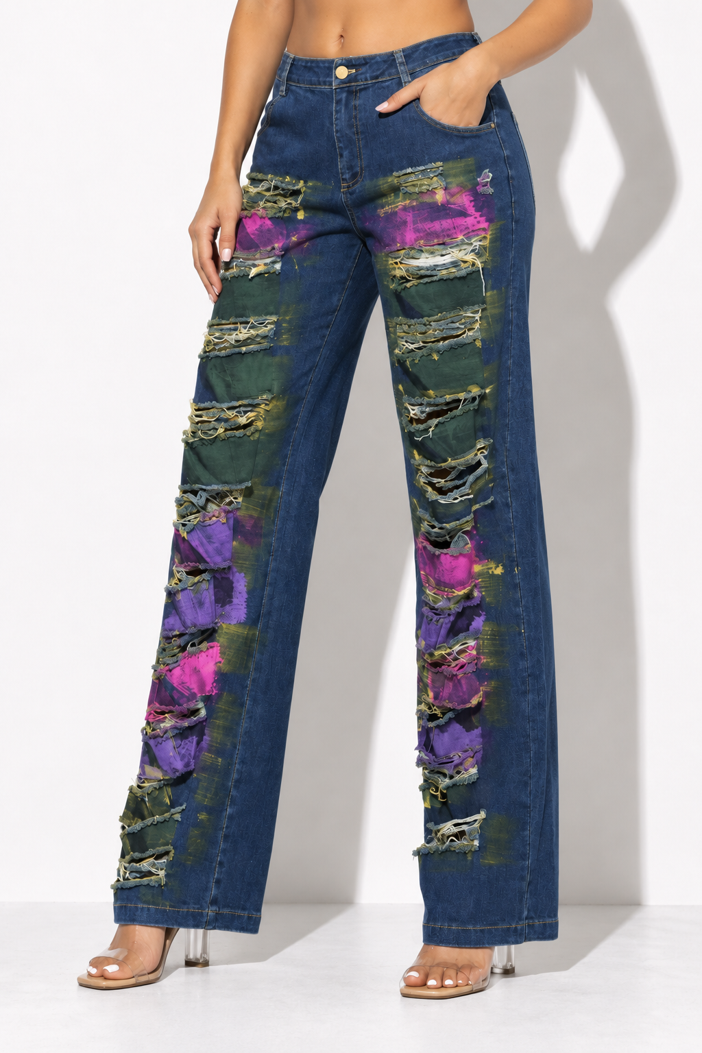 Distressed blue denim wide leg pants with pink and purple paint accents, angled front view showing relaxed straight legs